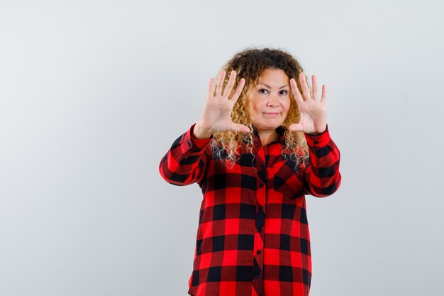 Foto grátis retrato de uma mulher loira bonita mostrando um gesto de parada em uma camisa quadriculada e parecendo descontente com a vista frontal