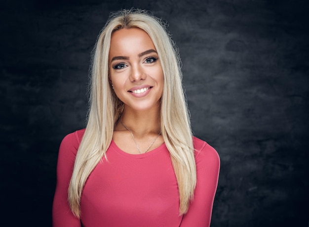 Foto grátis retrato de uma mulher loira sorridente, vestida com uma camisa esportiva rosa sobre fundo cinza.