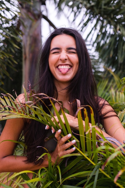 Retrato de uma mulher magra e bronzeada em forma de biquíni verde, posando com folhas tropicais