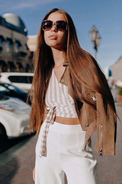 Retrato de uma mulher moderna elegante e feliz posando na rua em um dia ensolarado de verão sob a luz do sol