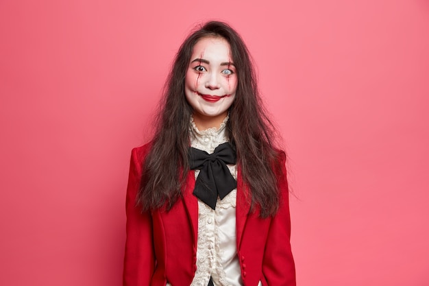 Retrato de uma mulher morena assustadora usando maquiagem gótica de halloween e imagens de um vampiro assustador indo para a festa com poses de olhar horrível contra uma parede rosada