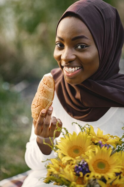 Retrato de uma mulher muçulmana sentada perto do rio comendo croissant