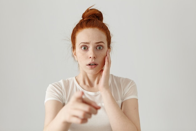 Retrato de uma mulher ruiva com medo de olhos esbugalhados, que tem uma expressão de medo aterrorizada, assustada com alguma coisa enquanto aponta o dedo indicador. Perigo, risco, acusação ou reconhecimento