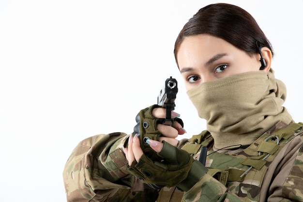 Foto grátis retrato de uma mulher soldado com arma em camuflagem de parede branca