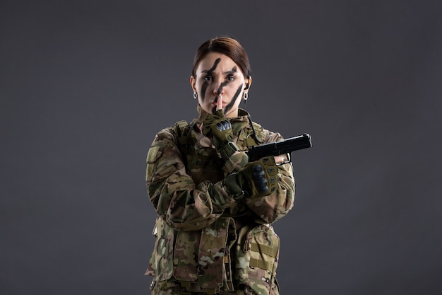 Retrato de uma mulher soldado com arma na camuflagem de parede escura