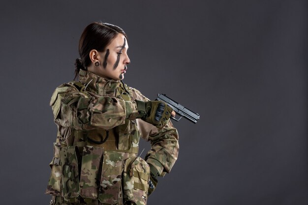 Retrato de uma mulher soldado com arma na camuflagem de parede escura