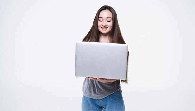 Retrato de uma mulher sorridente asiática segurando um laptop isolado na parede cinza