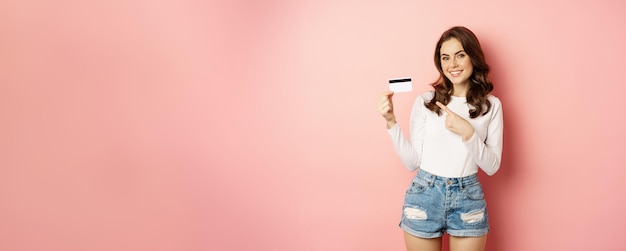 Foto grátis retrato de uma mulher sorridente atraente mostrando cartão de crédito recomendando loja de aplicativos com suporte de descontos