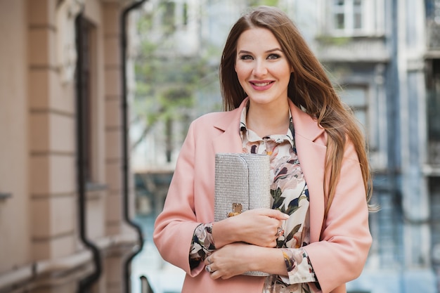 Retrato de uma mulher sorridente e atraente caminhando pelas ruas da cidade com casaco rosa e vestido floral