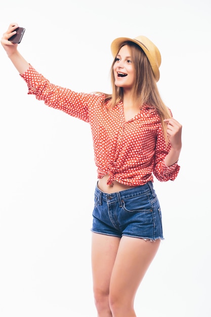 Retrato de uma mulher sorridente e fofa fazendo selfie em um smartphone isolado em um fundo branco