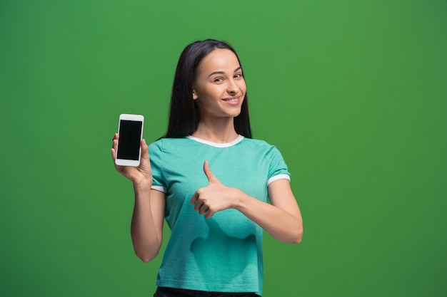 Retrato de uma mulher sorridente, mostrando a tela do smartphone em branco, isolada em um fundo verde