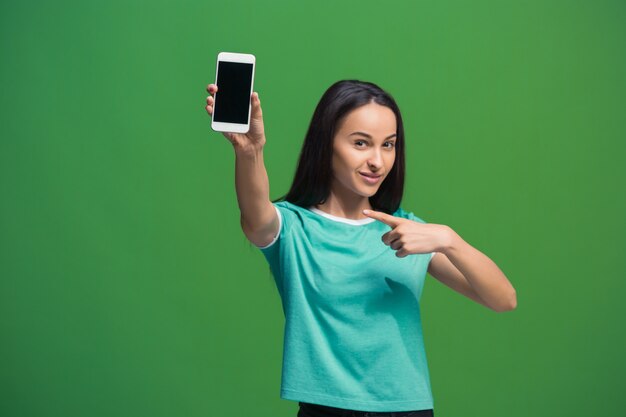 Retrato de uma mulher sorridente, mostrando a tela em branco do smartphone isolada em um verde