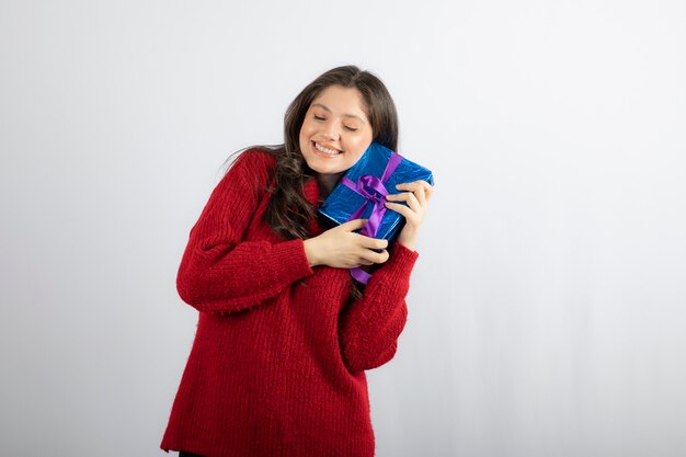 Retrato de uma mulher sorridente, segurando uma caixa de presente de natal com fita roxa.