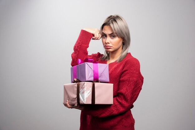 Retrato de uma mulher triste segurando caixas de presente em fundo cinza.