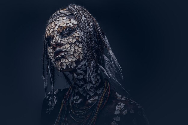 Retrato de uma mulher xamã africana assustadora com uma pele rachada petrificada e dreadlocks em um fundo escuro. Conceito de maquiagem.