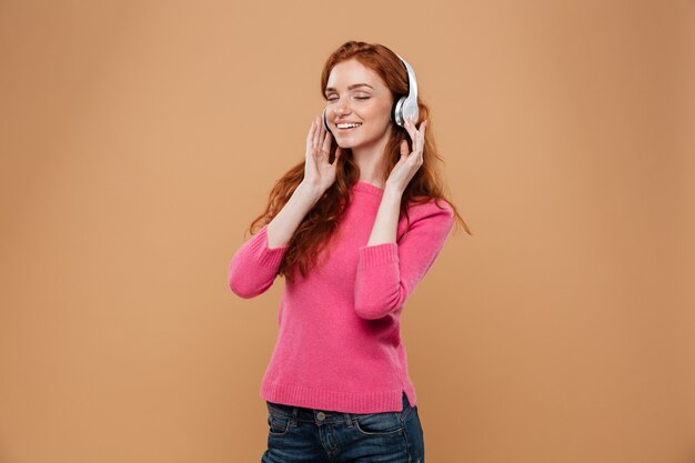 Retrato de uma música ruiva sorridente satisfeito garota ruiva com fones de ouvido
