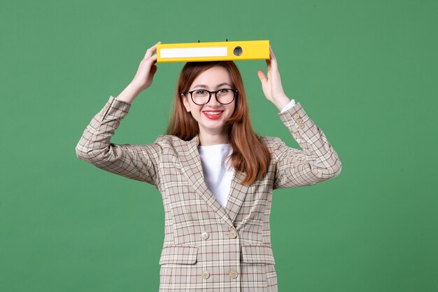 Retrato de uma professora segurando um documento amarelo na cabeça verde