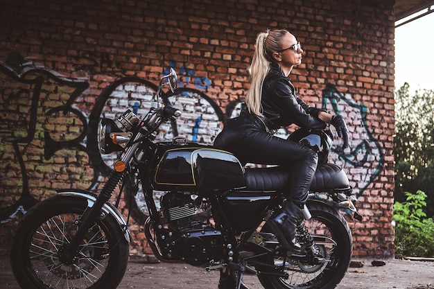 Retrato de uma senhora atraente madura ao lado de sua moto vintage e parede de tijolos de graffiti.