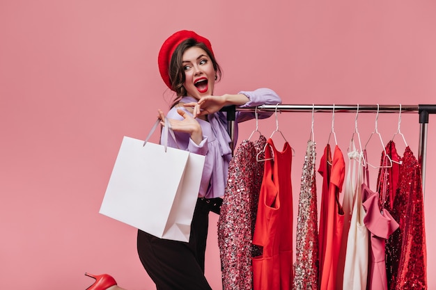 Foto grátis retrato de uma senhora brilhante com batom vermelho, posando alegremente com o pacote, enquanto fazia compras no fundo rosa.