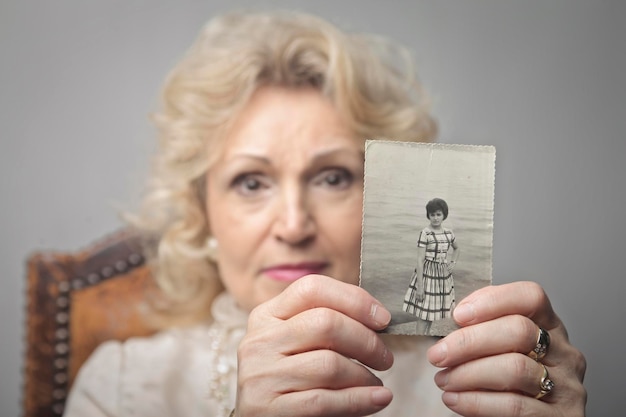 Retrato de uma senhora idosa com uma foto na mão de quando ela era jovem