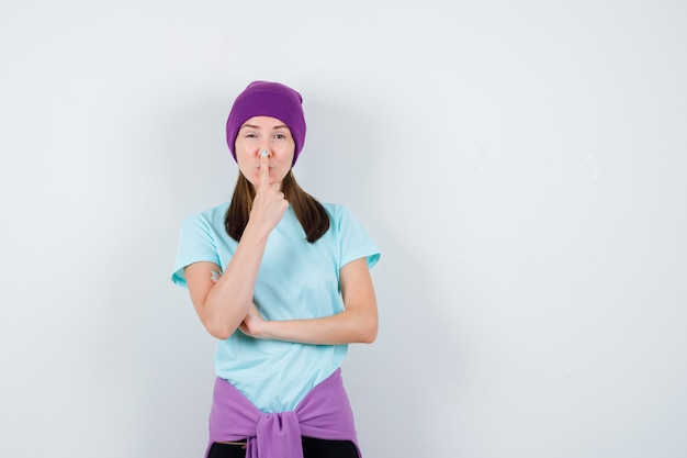 Retrato de uma senhora maravilhosa mantendo o dedo no nariz na blusa, gorro e olhando de frente positivamente