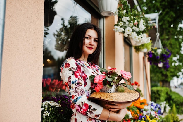 Retrato de verão da menina morena de óculos cor de rosa e chapéu contra loja de flores