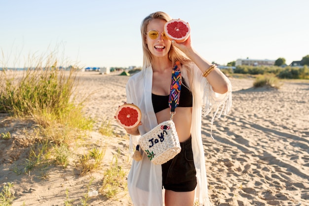 Retrato de verão da mulher despreocupada brincalhão, posando com saborosas metades de toranja nas mãos.