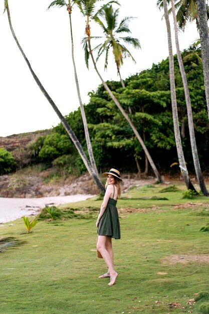 Retrato de verão exótico de mulher bonita loira posando na ilha exótica, usando vestido e chapéu de palha. Férias de luxo na ilha.