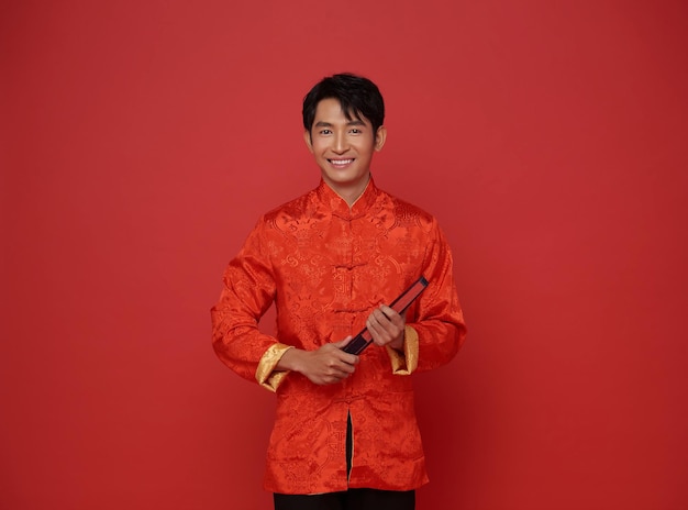 Foto grátis retrato do ano novo chinês de 2024 homem asiático sorrindo vestindo roupas tradicionais vermelhas segurando um ventilador vermelho