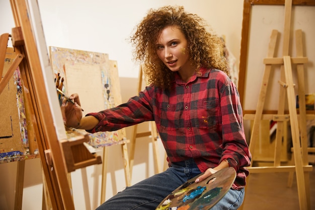 Retrato do artista encaracolado ruiva linda durante seu trabalho