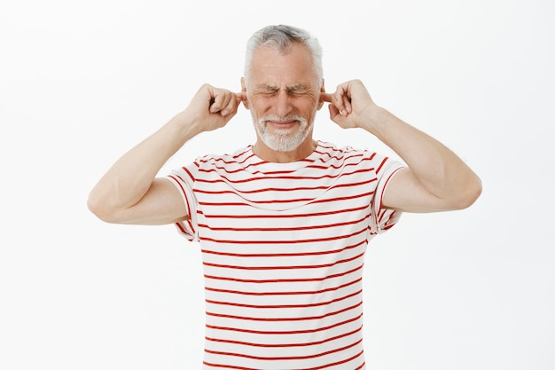 Retrato do avô descontente fechando os ouvidos com os dedos e fazendo caretas devido ao barulho alto