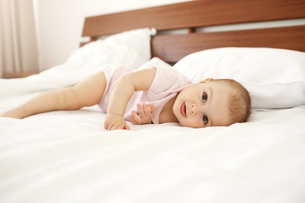 Retrato do bebê recém-nascido bonito bonito que mostra a língua que encontra-se na cama em casa.