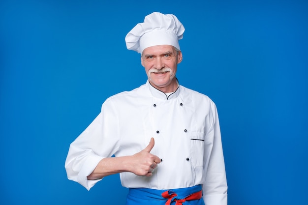 Retrato do chef idoso isolado na parede azul, com gesto de ok