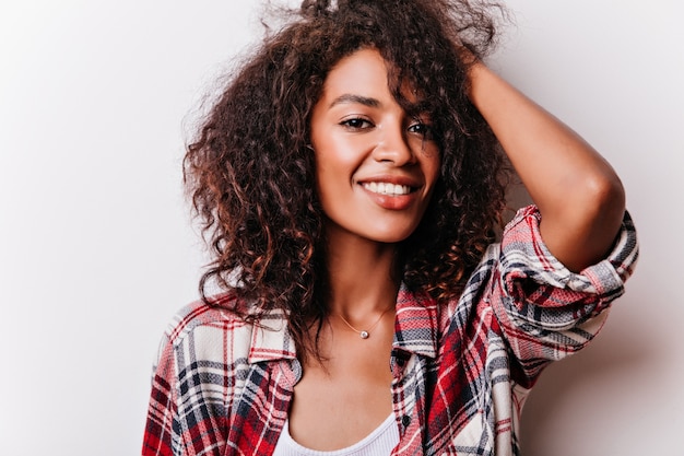 Foto grátis retrato do close-up da adorável garota negra tocando seus cabelos ondulados. modelo feminino positivo usa a camisa quadriculada da moda.