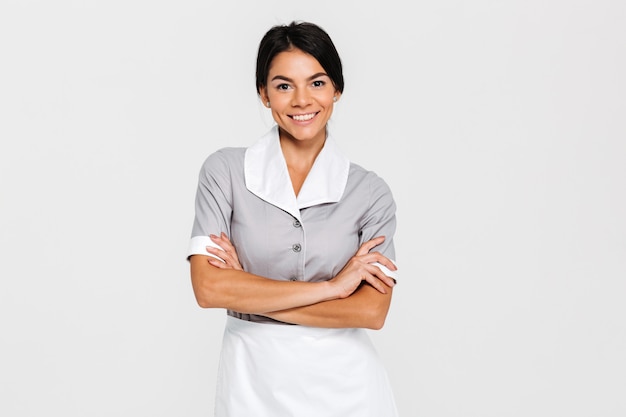 Retrato do close-up da jovem empregada sorridente em uniforme em pé com as mãos cruzadas