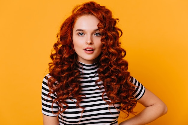 Foto grátis retrato do close-up da menina de olhos azuis com cílios longos e volumoso cabelo ruivo cacheado contra o espaço laranja.