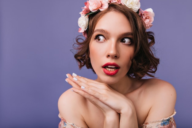 Retrato do close-up da mulher sonhadora bonita com rosas no cabelo. Foto interna de uma garota maravilhosa em pé de grinalda.