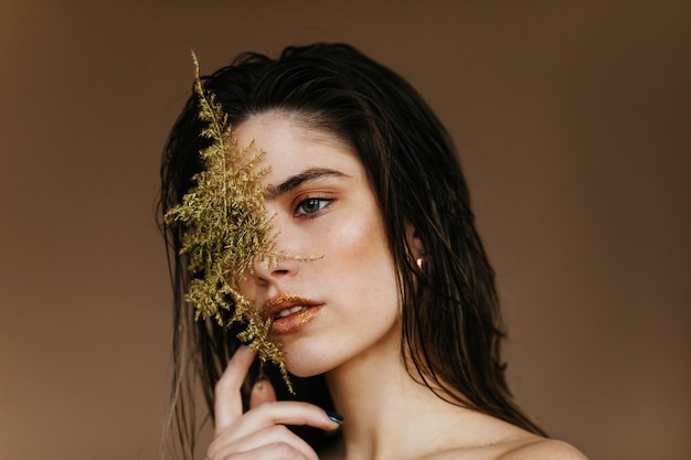 Retrato do close-up de adorável menina morena com planta. incrível modelo feminino segurando folha verde.