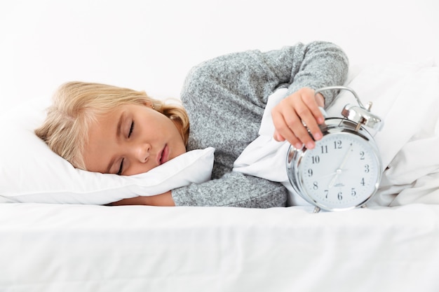Retrato do close-up de criança dormindo segurando o relógio despertador