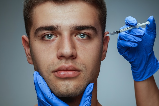 Retrato do close-up de jovem isolado em fundo cinza. Procedimento de cirurgia de enchimento.