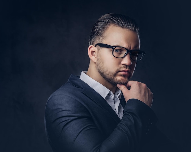 Retrato do close-up de um empresário elegante pensativo com cara séria em um elegante terno formal e óculos. Isolado em um fundo escuro.