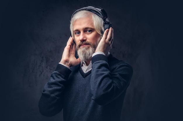 Retrato do close-up de um homem bonito sênior ouvindo música em fones de ouvido. Isolado um fundo escuro.