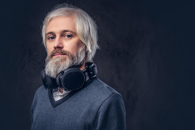 Retrato do close-up de um homem bonito sênior ouvindo música em fones de ouvido. Isolado um fundo escuro.