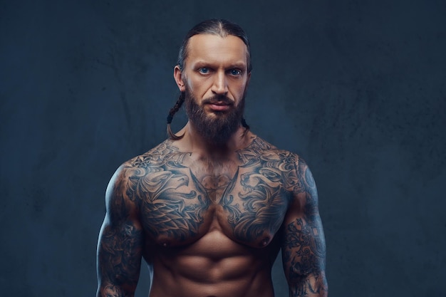 Retrato do close-up de um homem tatuado barbudo musculoso com um corte de cabelo elegante. Isolado em um fundo escuro.