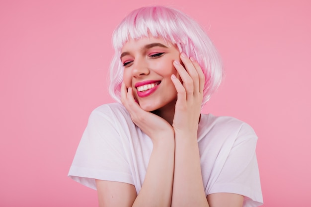 Retrato do close-up de uma agradável garota caucasiana com maquiagem da moda, posando de peruca rosa. Modelo feminino branco atraente com peruca rindo durante a sessão de fotos
