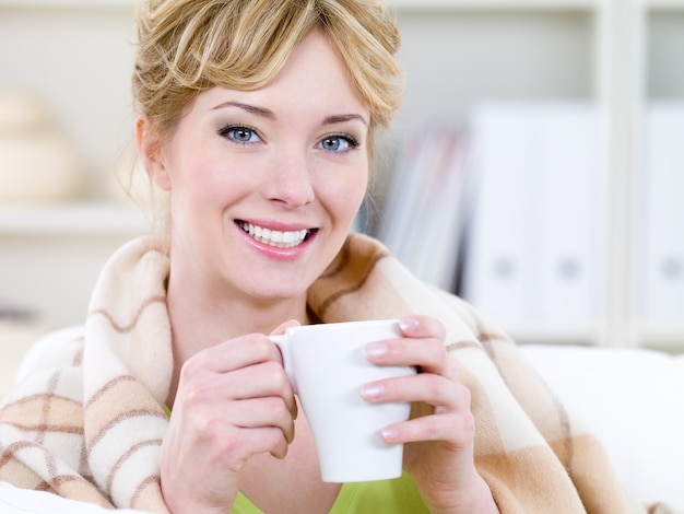 Retrato do close-up de uma bela jovem sorridente e feliz se aquecendo com uma xícara de café quente