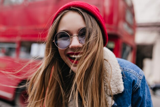 Retrato do close-up de uma jovem magnífica com cabelo escuro, rindo na rua. Tiro ao ar livre da garota emocional na jaqueta jeans, se divertindo no fim de semana de primavera, enquanto relaxa na cidade.