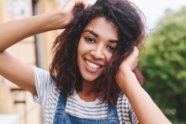 Retrato do close-up de uma jovem morena com pele bronzeada posando com prazer ao ar livre e sorrindo