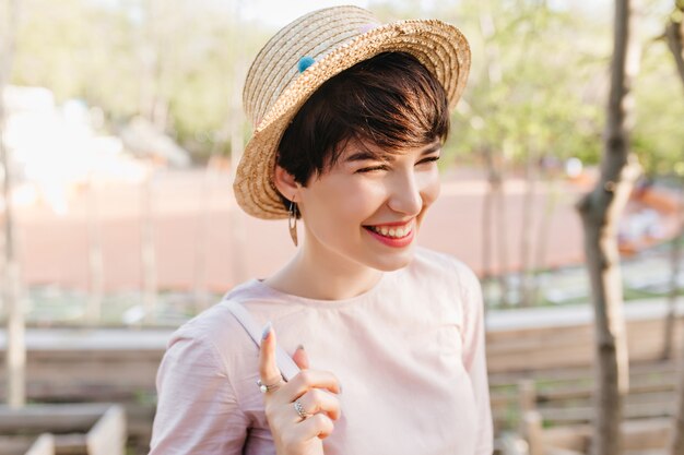 Retrato do close-up de uma menina sorridente, usando um chapéu de palha da moda e anéis, caminhando ao ar livre depois do almoço