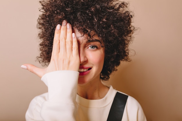 Retrato do close-up de uma mulher jovem e bonita com penteado curto e grandes olhos azuis fechados de um lado do rosto com a mão em bege